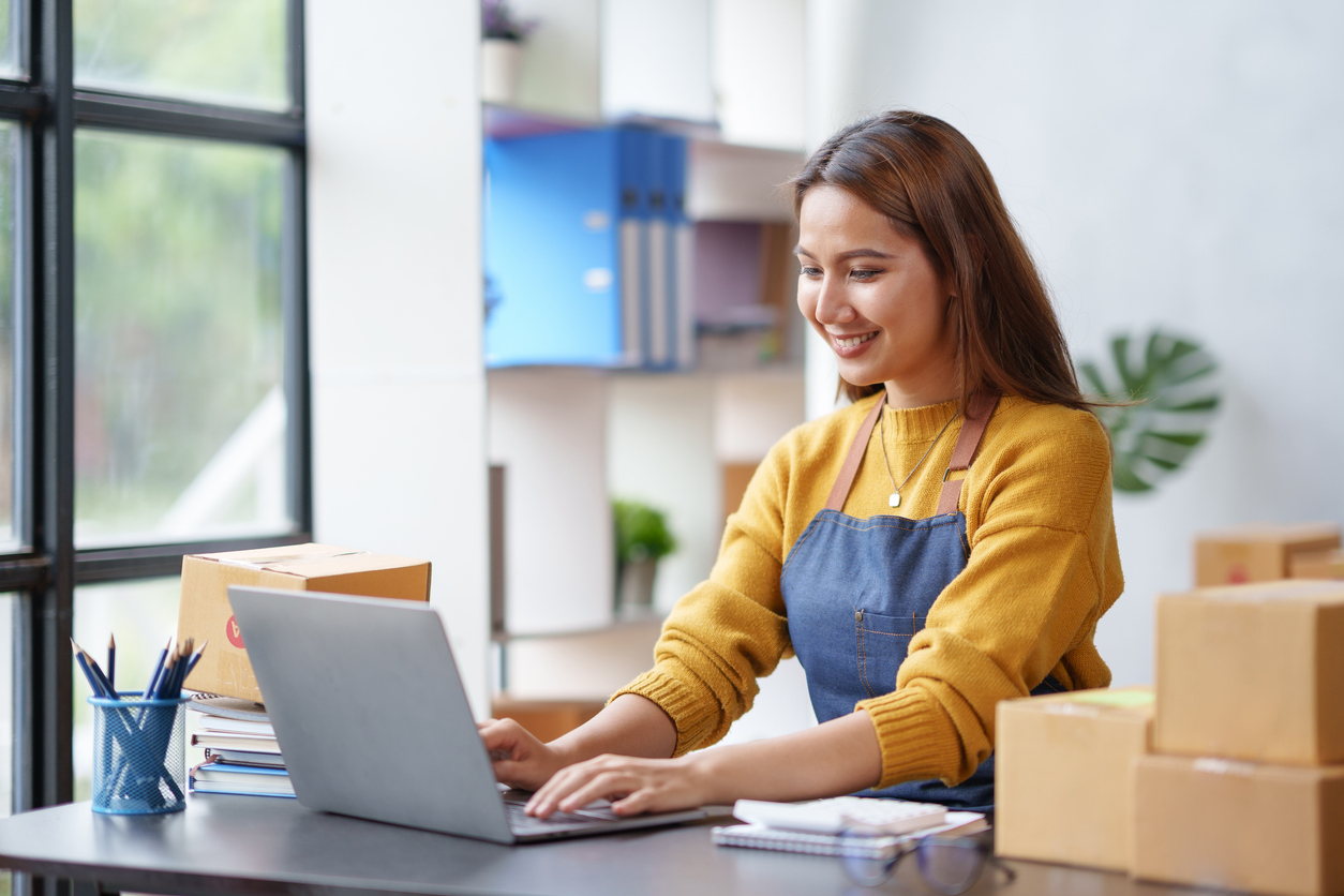 happy young asian business owner woman prepare parcel box and check online orders of product for deliver to customer on laptop computer. shopping online concept.